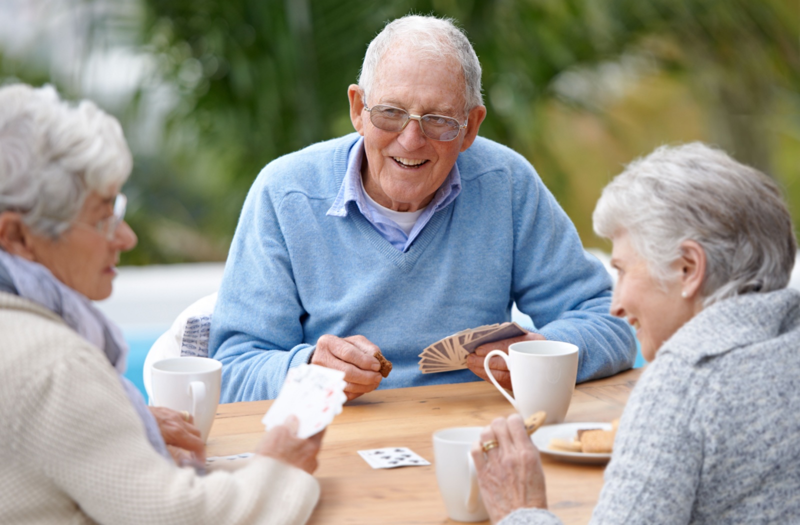 Three seniors sitting at a table playing cards and smiling
