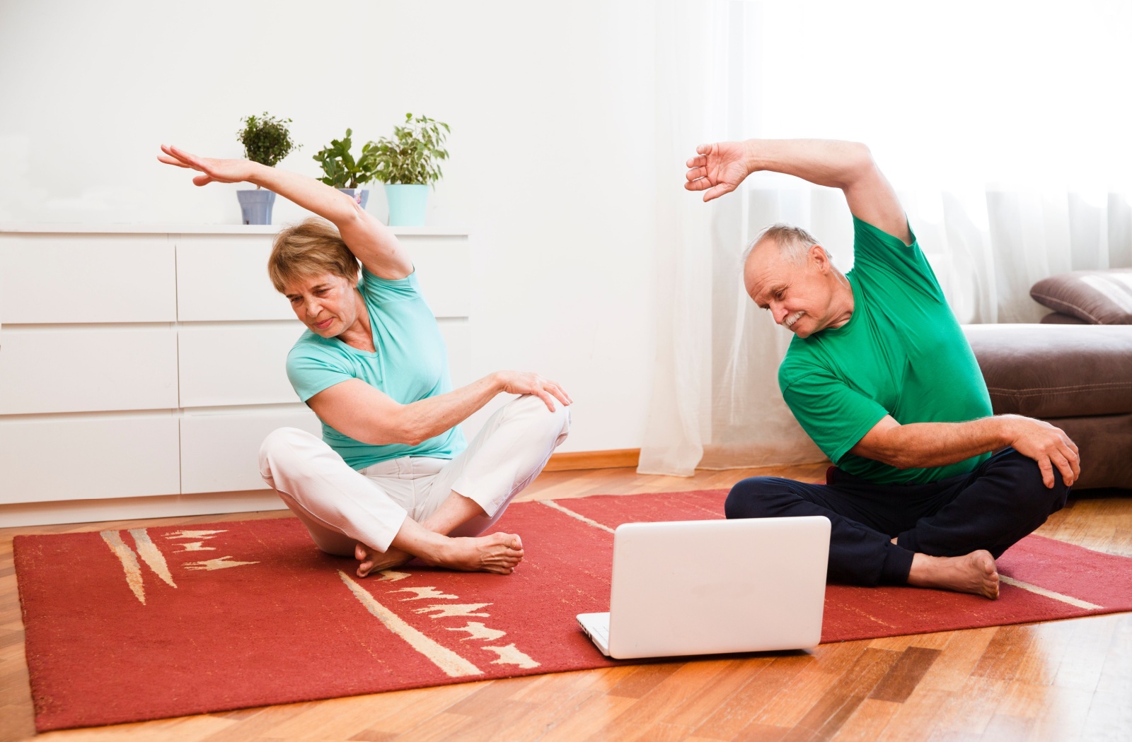 A mature couple seated on the floor as they perform their side bends.