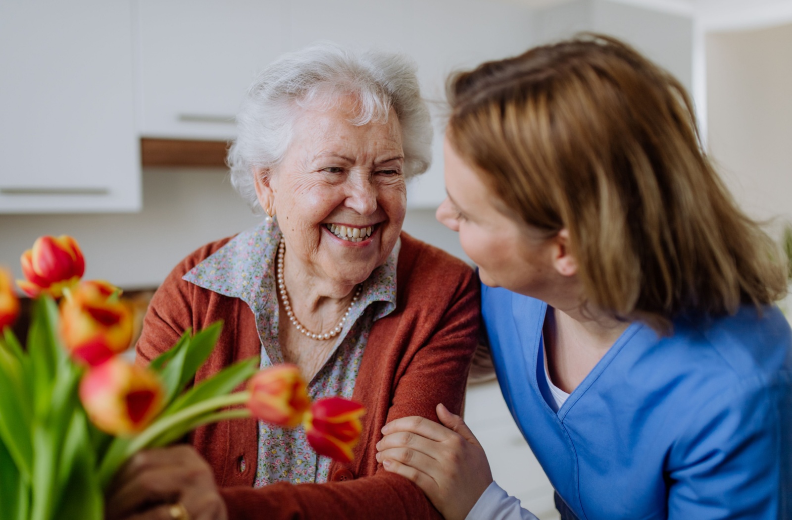 A senior living in memory care smiles at their nurse while arranging tulips.