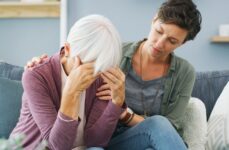 A stressed daughter holds her elderly mother, which is clutching her head in her hands.