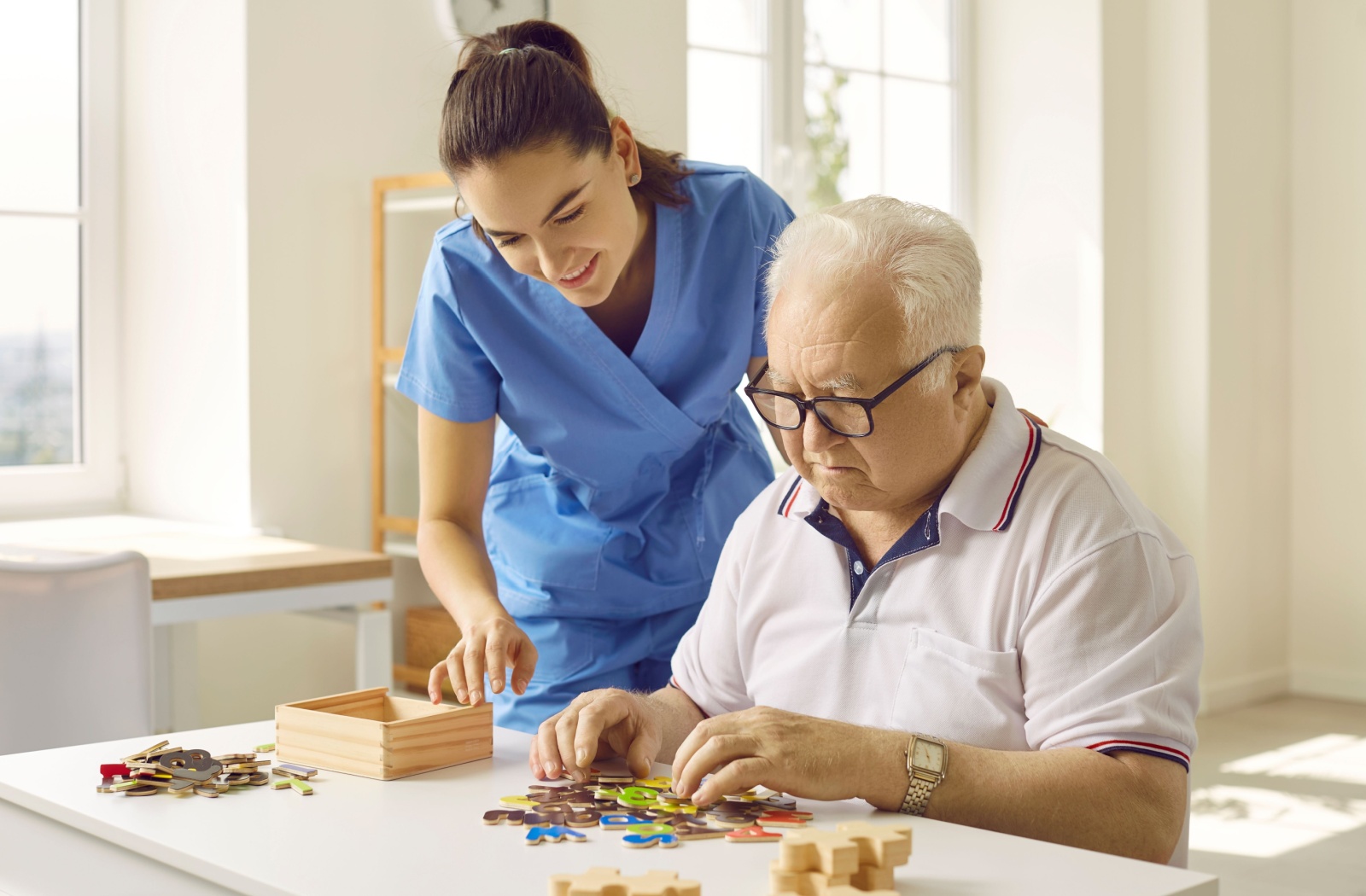 A friendly caregiver assists an elderly man with his puzzle.
