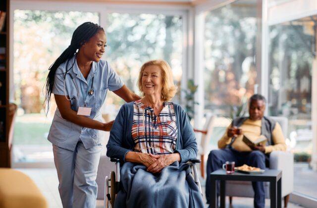 A nurse pushes a smiling senior in their wheelchair around their assisted living community.