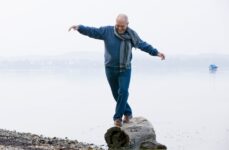 A senior balances on a lakeside log with confidence and joy.